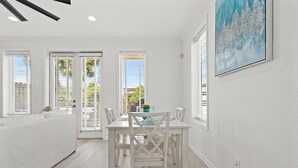 A bright, white interior with a dining table and chairs, large windows with blinds, and a painting on the wall. - Spacious 4BR • Pool • Arcade • Walk to Beach • BBQ (Panama City Beach)