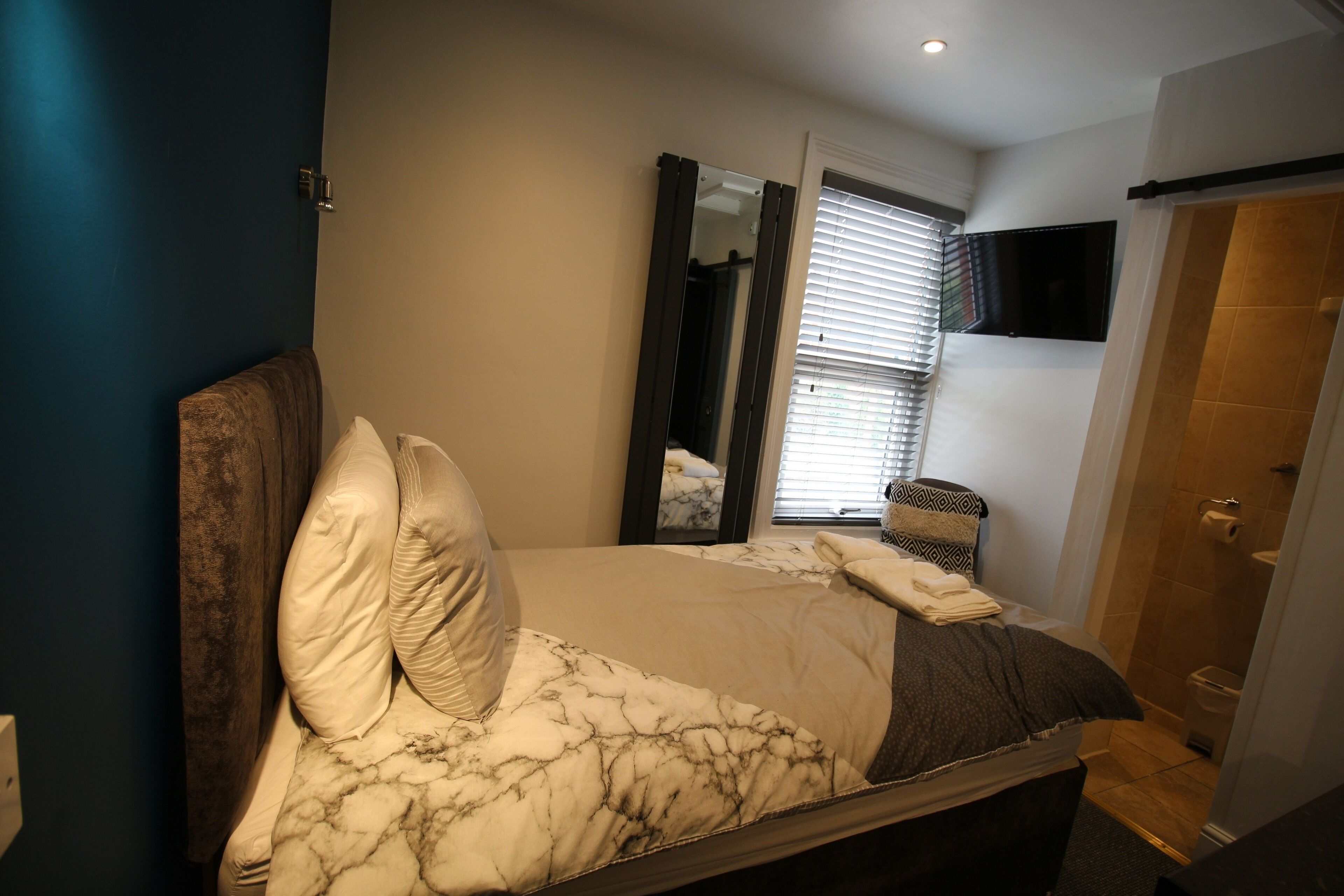 Un dormitorio con cama, un espejo grande, televisor y zona de ducha.