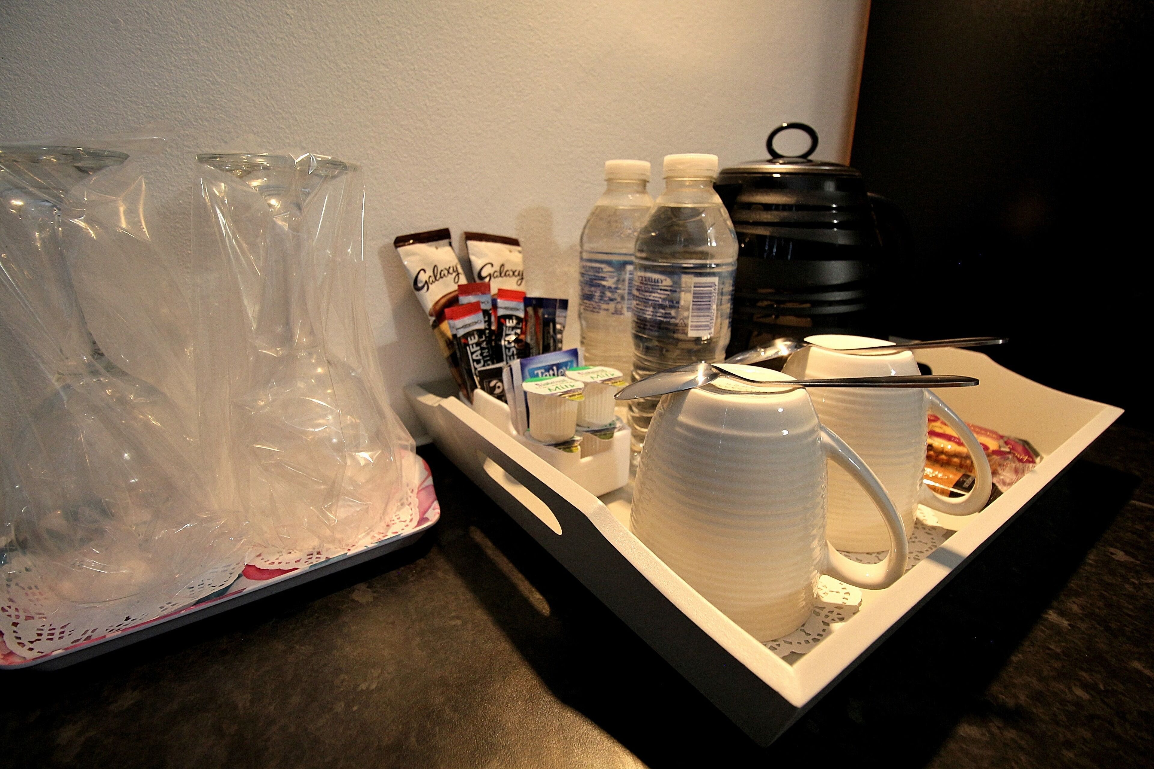 A tray with a coffee maker, cups, a water bottle, and some snacks.