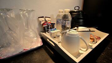 A tray with a coffee maker, cups, a water bottle, and some snacks.