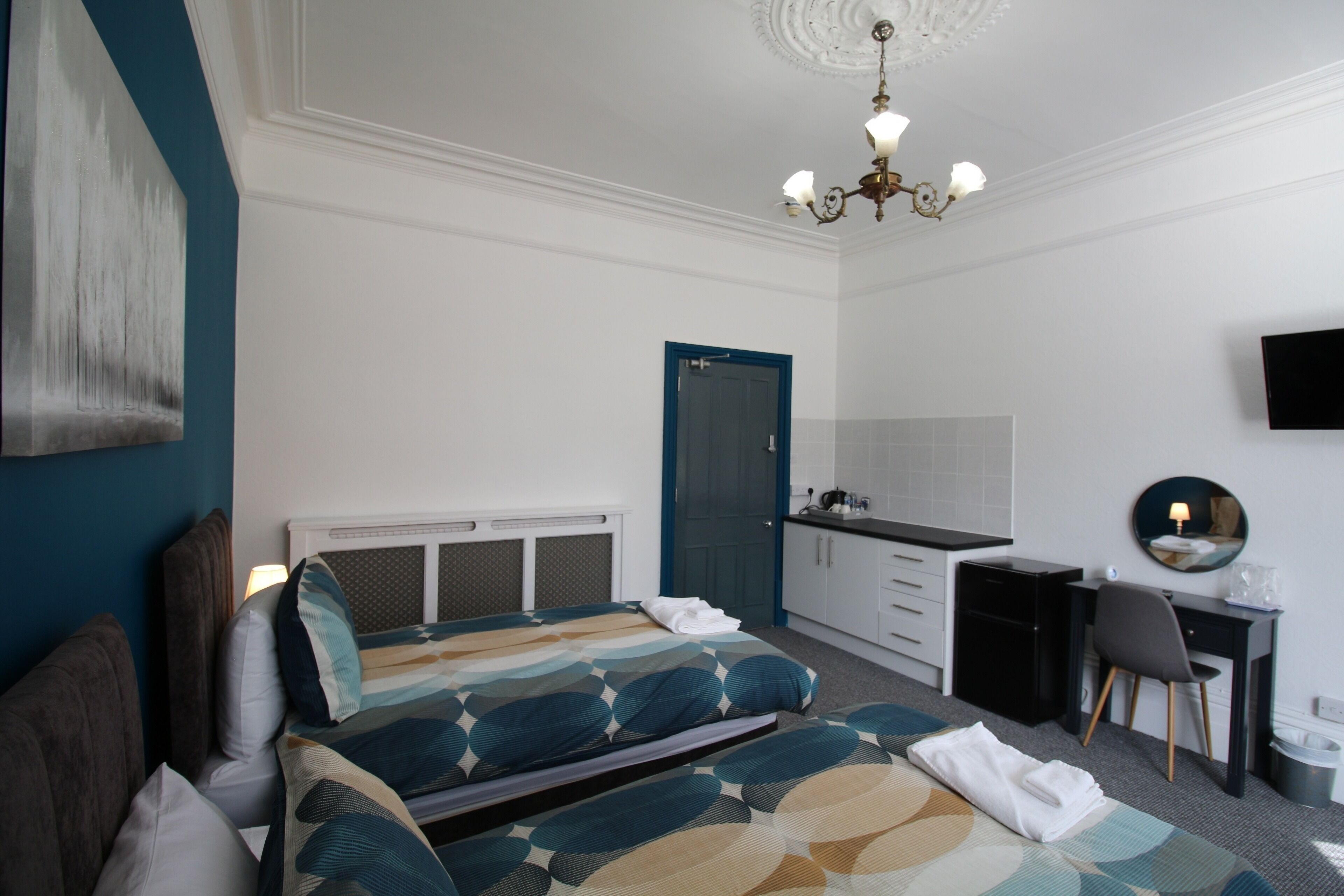 Quarto de hotel com cama, escrivaninha, cadeira, televisão e porta.