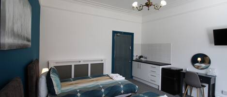 Quarto de hotel com cama, escrivaninha, cadeira, televisão e porta.