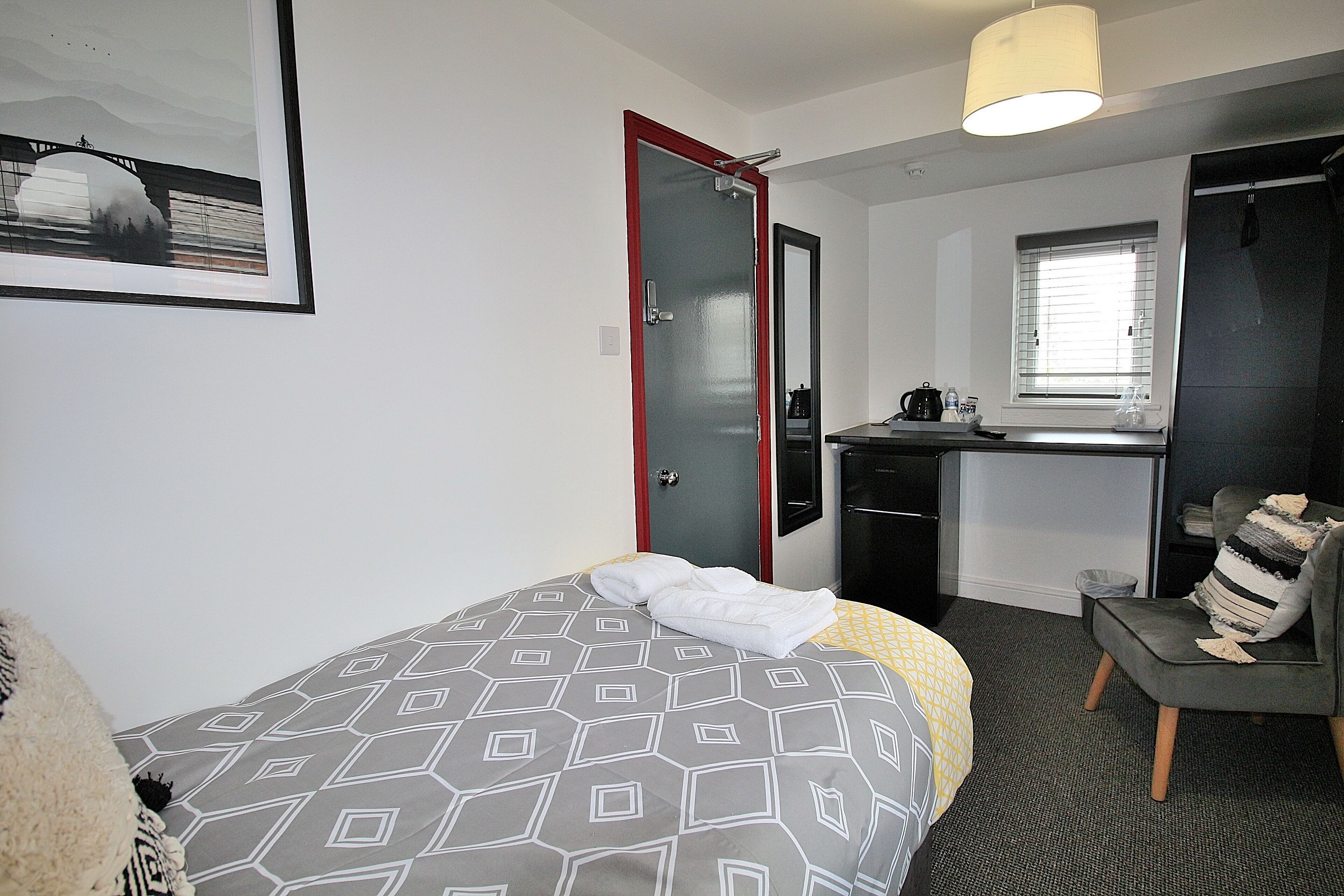 Une chambre d’hôtel avec un lit, un bureau, une chaise et une fenêtre.