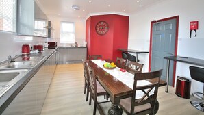 Une cuisine moderne dotée d’appareils électroménagers en acier inoxydable, une table à manger pour quatre personnes et un mur d’accent rouge.
