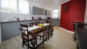 Une cuisine moderne avec un coin repas, comprenant une grande table en bois, des chaises et un mur d’accent rouge agrémenté d’une horloge.