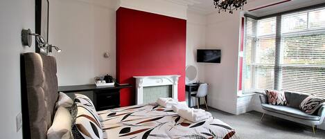 A bedroom with a bed, a desk, a chair, a sofa, and a TV.