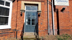 Un bâtiment en briques avec une porte bleu foncé portant l’inscription « Hamiltons » et une enseigne indiquant qu’il s’agit d’un hôtel agréé.