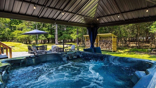 A hot tub area with a covered roof, lounge chairs, and a wooden structure in the background. - MountainTime Lodge at Towamensing Trails -Hot Tub - Fire Pit - Dog Friendly (Albrightsville)