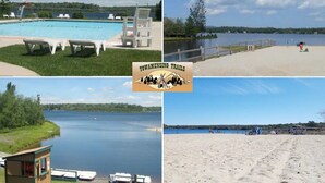 A swimming pool with lounge chairs, a lifeguard tower, and a beach area with a wooden structure and boats. - MountainTime Lodge at Towamensing Trails -Hot Tub - Fire Pit - Dog Friendly (Albrightsville)