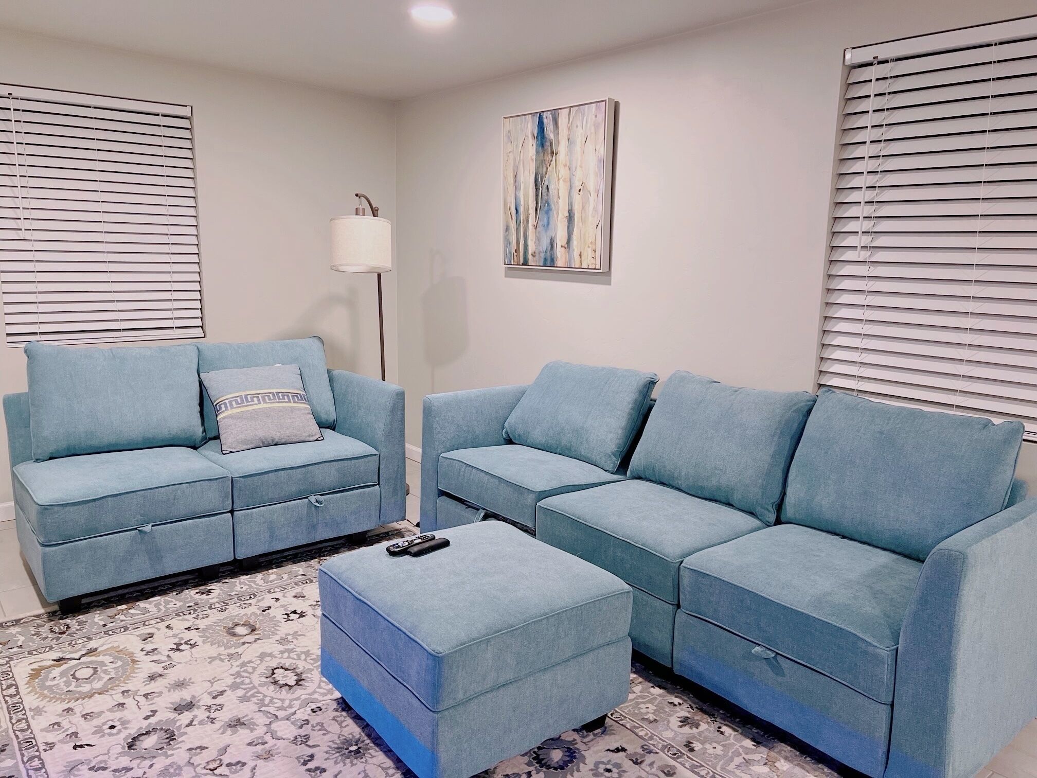 Uma sala de estar com dois sofás, uma mesa de centro, um abajur e um quadro na parede.