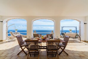 A dining area with a table set for four, overlooking a coastal view through arched openings. - Villa Petra by BarbarHouse (Gagliano del Capo)