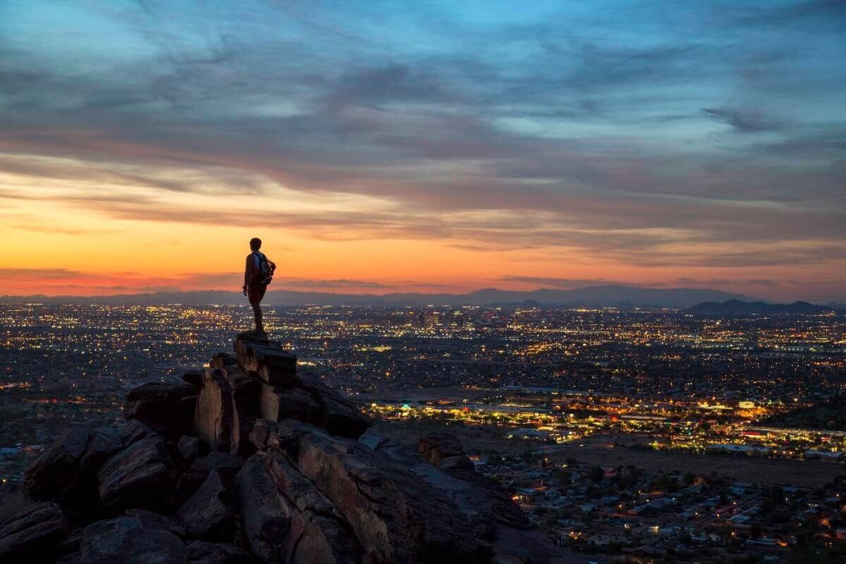 A person standing on a rocky outcrop overlooking a cityscape at dusk.