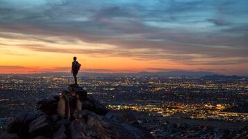 A person standing on a rocky outcrop overlooking a cityscape at dusk.