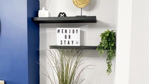 Un interior moderno con una pared azul de acento, una estantería con adornos, un cartel con texto motivacional y una planta en maceta.