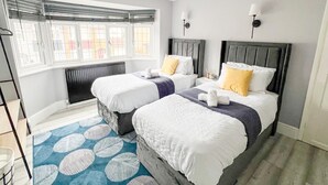 Habitación de hotel con dos camas, un ventanal amplio, un radiador y un tapete azul estampado.