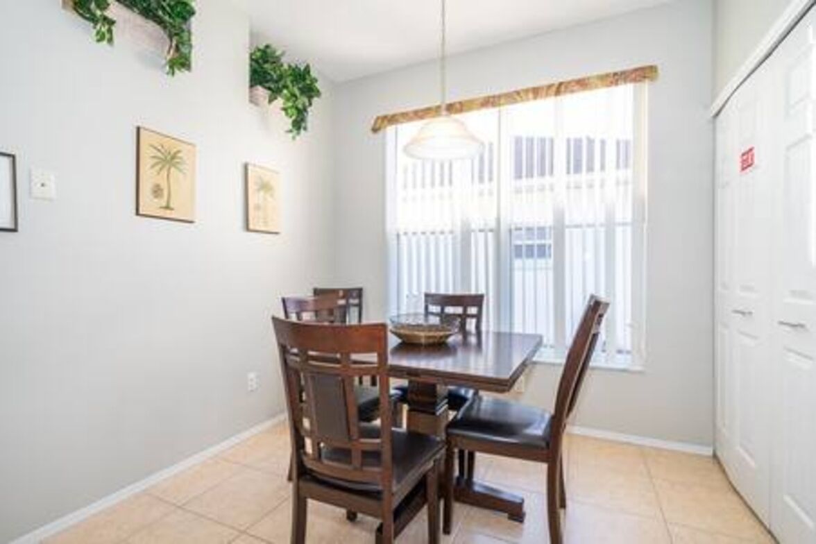 A dining area with a wooden table and chairs, a hanging light fixture, and a window with blinds.