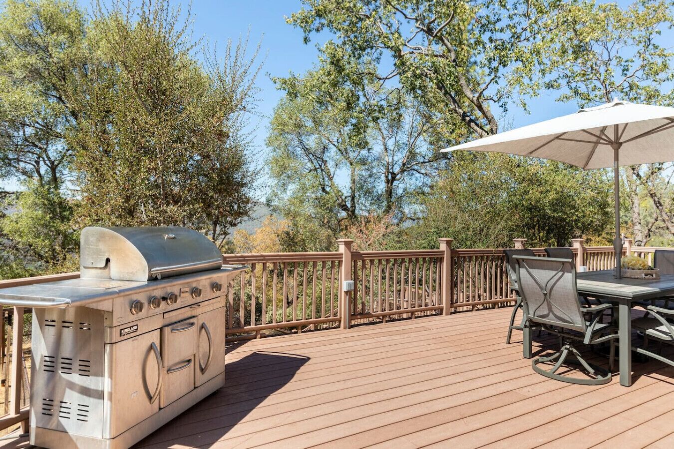 An outdoor deck with a grill, dining table, chairs, and an umbrella.