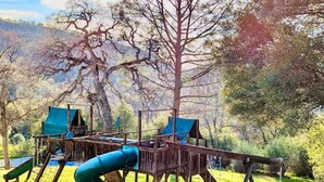 Un parque infantil con tobogán y estructuras para escalar, rodeado de árboles y césped.