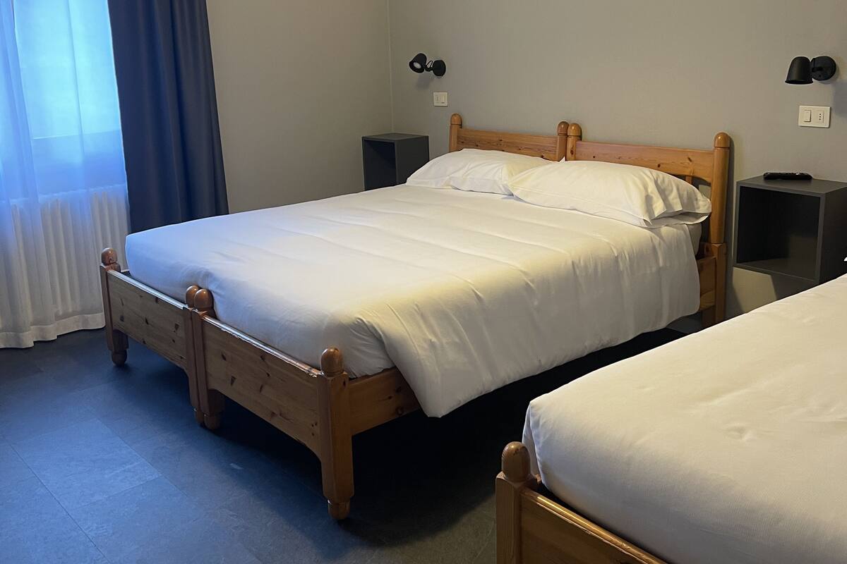 A hotel room with two wooden beds, a ceiling light, a nightstand, and a window with curtains.