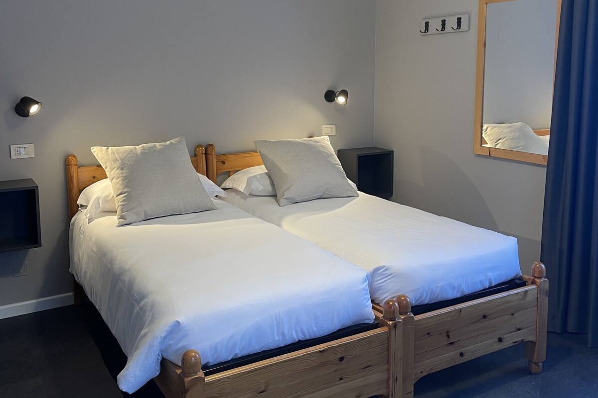 A double bed with wooden headboard and footboard, two bedside tables, a wall-mounted light fixture, and a mirror with a wooden frame.