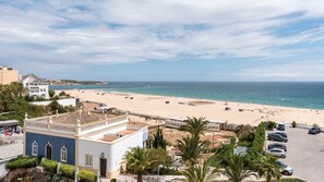 A coastal view with a beach, a parking area, and a building with a tiled roof.