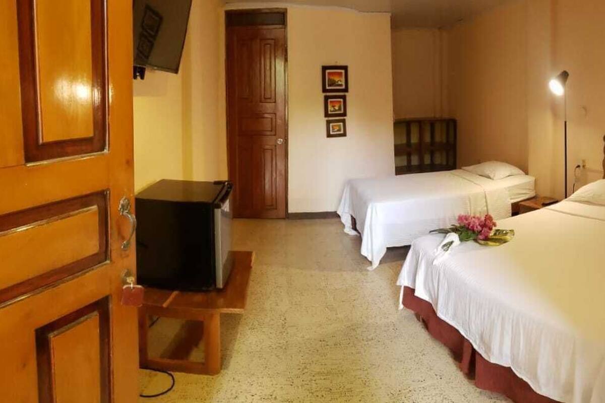 A hotel room with two single beds, a wooden wardrobe, a desk with a television, and a small table with a vase of flowers.
