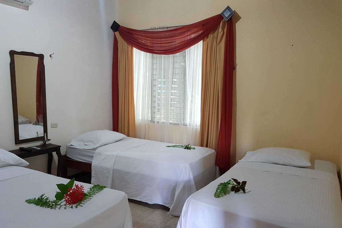 A hotel room with two single beds, a nightstand, a mirror, and a window with curtains.