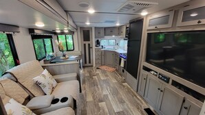 A compact RV interior with a kitchenette, seating area, and entertainment system. - New little getaway (Fernandina Beach)