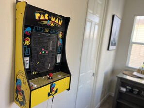 Una máquina arcade de Pac-Man montada en una pared en una habitación con una puerta y una ventana.