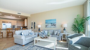 A living room with a sofa, coffee table, and a painting of a beach scene. - Two Bedroom Penthouse with Balcony Overlooking Pool Decks and Gulf. Complimentary Boat Slip! (Orange Beach)