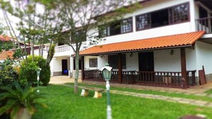 A two-story house with a red-tiled roof, a balcony, and a small garden area with a lawn and a few potted plants. - Space 579 is the ideal place for you and your family! (Miguel Pereira)