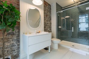 Un bagno moderno con un vanità bianca, uno specchio rotondo, un water e una cabina doccia in vetro.