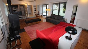 A modern living room with a red sofa, a grey couch, and a black TV stand. - Casa do Rio Vez - LOFT IN RIVERFRONT (Arcos de Valdevez)