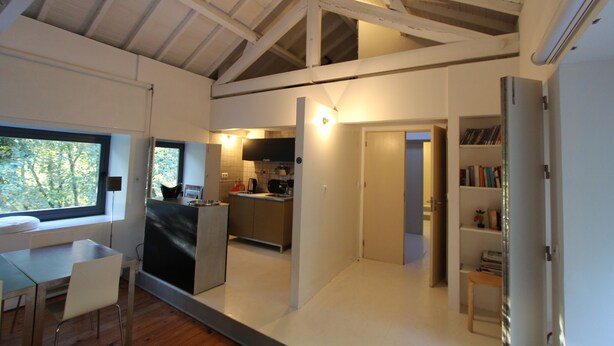 A modern interior with a kitchen, dining area, and a bookshelf. - Casa do Rio Vez - LOFT IN RIVERFRONT (Arcos de Valdevez)