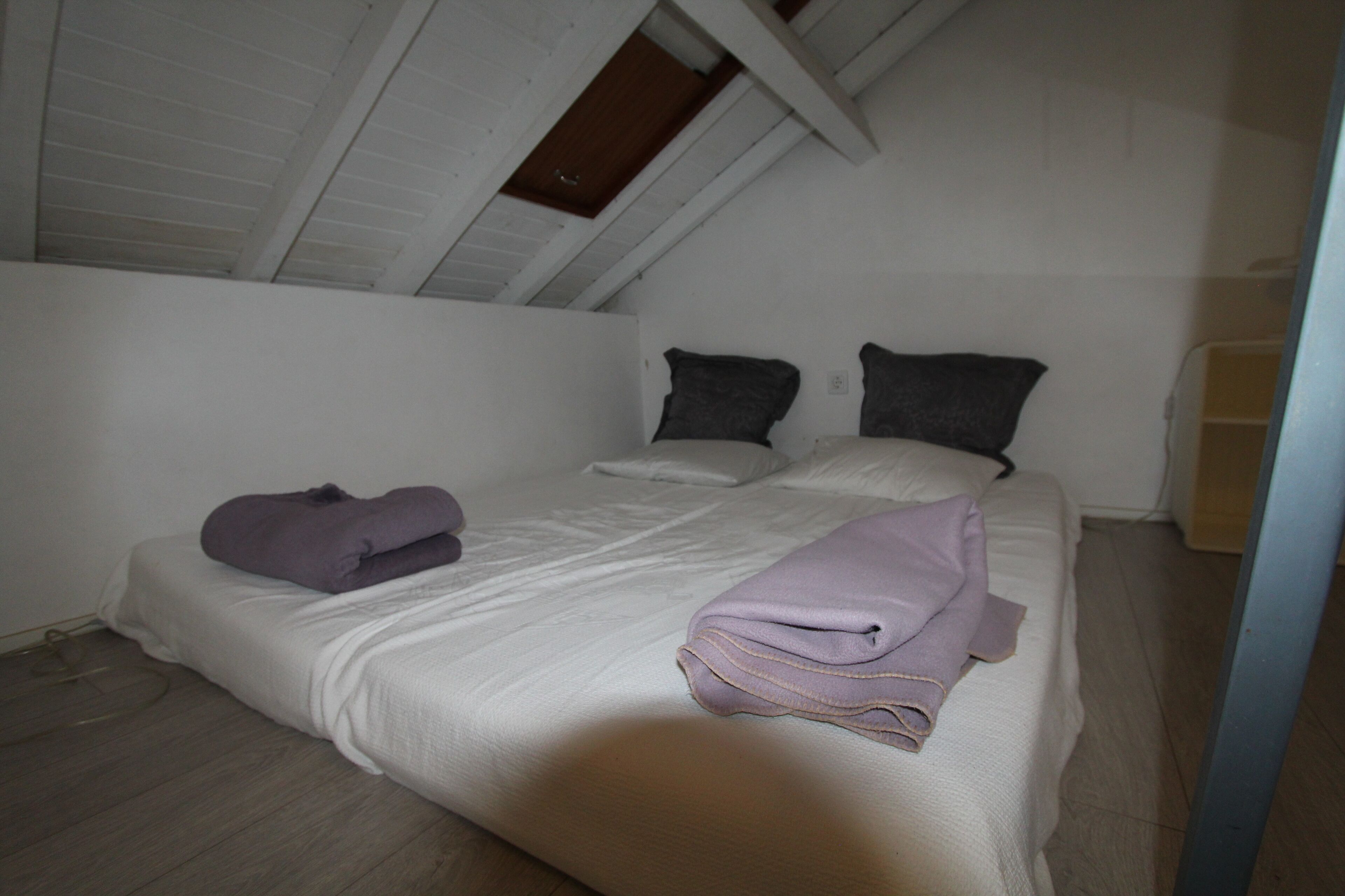 Una cama individual con colchón blanco y dos almohadas, una toalla doblada y una manta en el suelo.