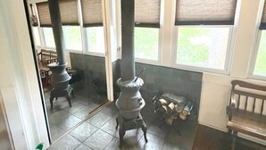 A room with a wood-burning stove, a bench, and a window with blinds. - Lake Luzerne Cottage with Lake Rights 15 Min from Lake George (Lake Luzerne)