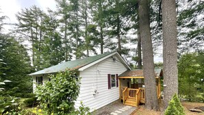 A small cabin with a porch, surrounded by dense trees and greenery. - Lake Luzerne Cottage with Lake Rights 15 Min from Lake George (Lake Luzerne)