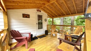 A wooden deck with Adirondack chairs and a bench, a door with a welcome sign, and a view of trees. - Lake Luzerne Cottage with Lake Rights 15 Min from Lake George (Lake Luzerne)