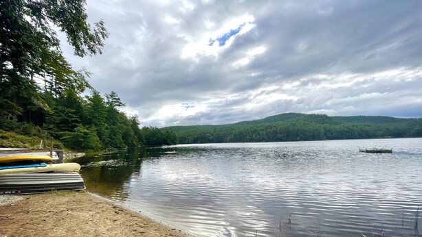 A lakeside view with a dock, kayaks, and a boat. - Lake Luzerne Cottage with Lake Rights 15 Min from Lake George (Lake Luzerne)