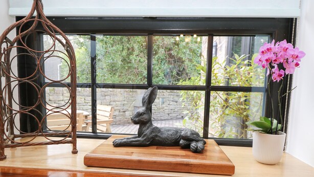 Uma mesa de madeira com uma escultura de coelho, uma decoração metálica pendente e uma orquídea em vaso.