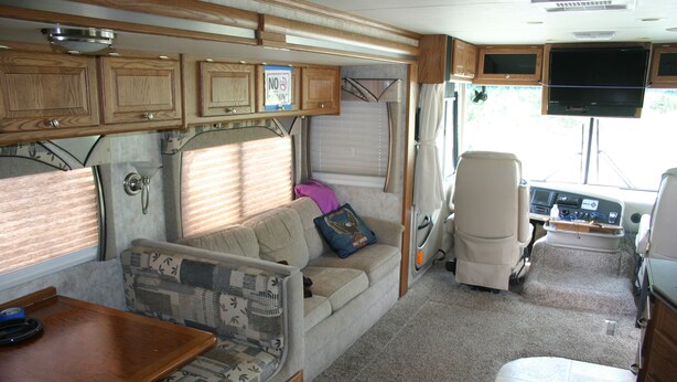 Een compact interieur van een camper, met een kitchenette, een bank, een eettafel en een televisie boven de zithoek.