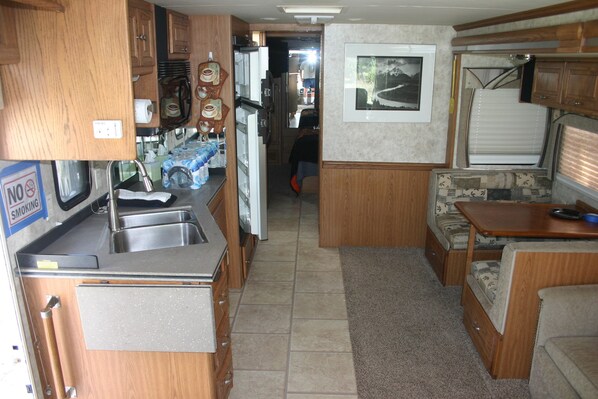 A compact RV kitchen with a sink, stove, and refrigerator. There is a dining area with a table and a couch.