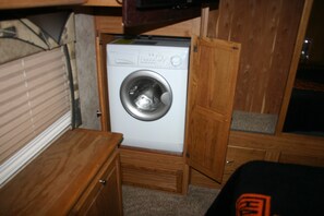 A compact laundry room with a washing machine, wooden cabinets, and a small wooden bench.