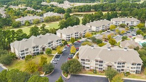 A multi-story residential building with a central courtyard, parking lot, and surrounding greenery. - 280-15 Woodlands Way (Calabash)