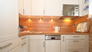 Eine kleine Küche mit weißen Schränken, einem Edelstahl-Geschirrspüler, einer Mikrowelle und einer Holzausziehtafel.