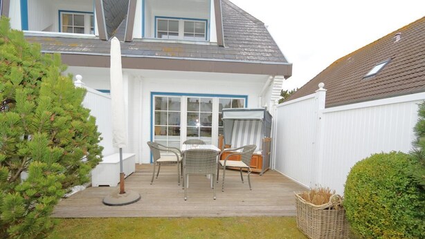 Ein Haus mit überdachter Terrasse, weißem Zaun und kleinem Garten.