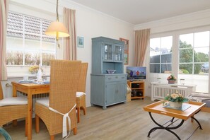 A cozy living room with wicker furniture, a blue cabinet, and a table with a flower arrangement. - Haus Sommer am Munkmarscher Strand (Munkmarsch)