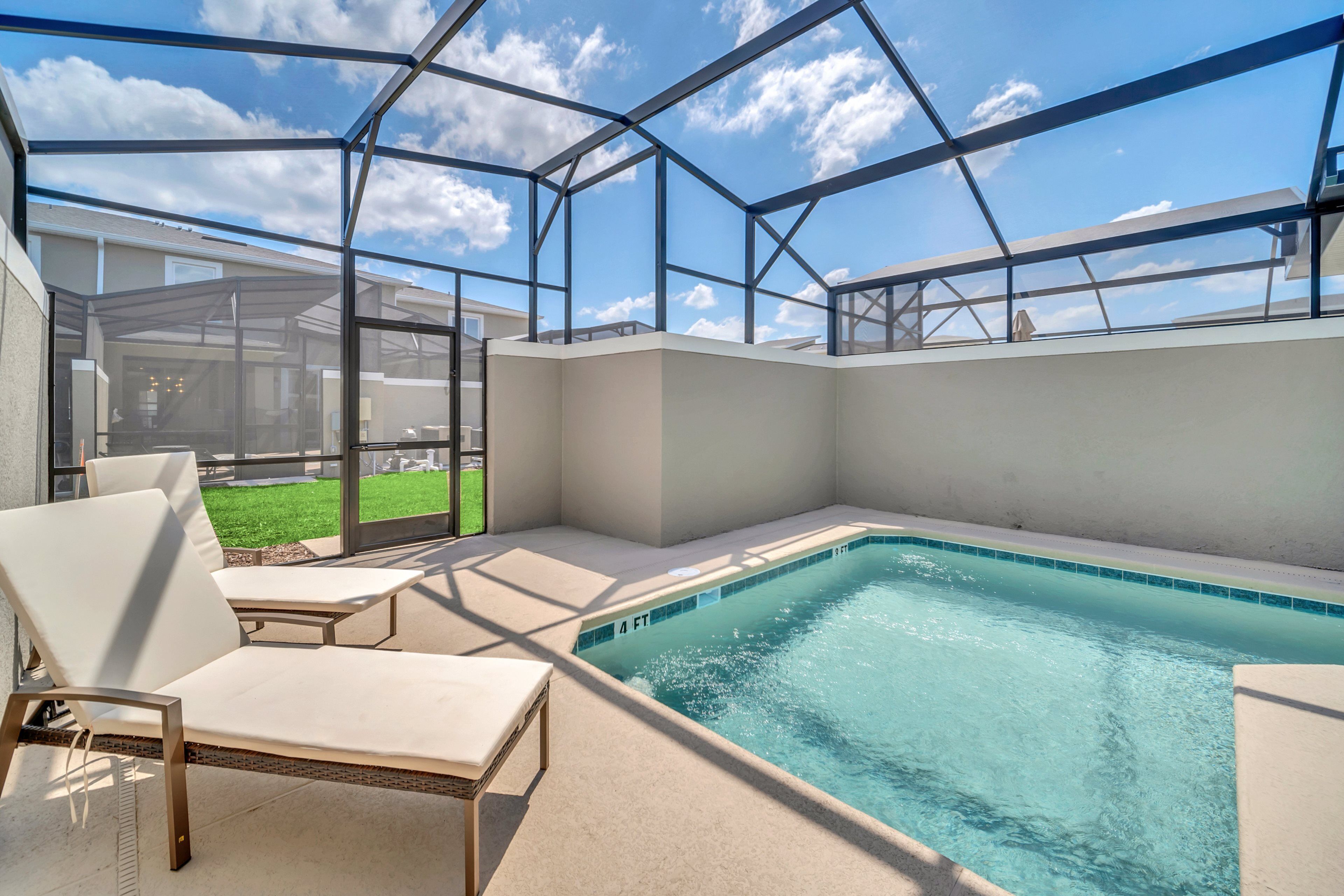 A swimming pool with a glass enclosure, lounge chairs, and a view of a grassy yard.