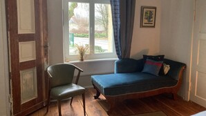 A room with a wooden floor, a green chair, a blue sofa, a window with a view of the outside, and a door. - No letting via FEWO (Lärz)