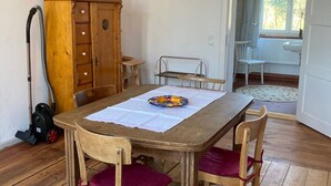 A dining area with a wooden table and chairs, a vacuum cleaner, a cabinet, and a window with a view of trees. - No letting via FEWO (Lärz)